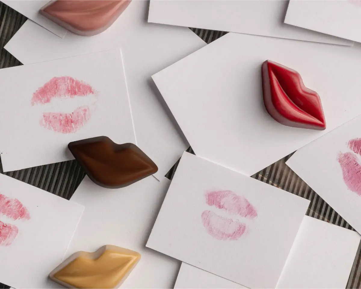 Cioccolatini a forma di labbra, rossi, fondenti e al caramello, fra biglietti bianchi coi baci di rossetto