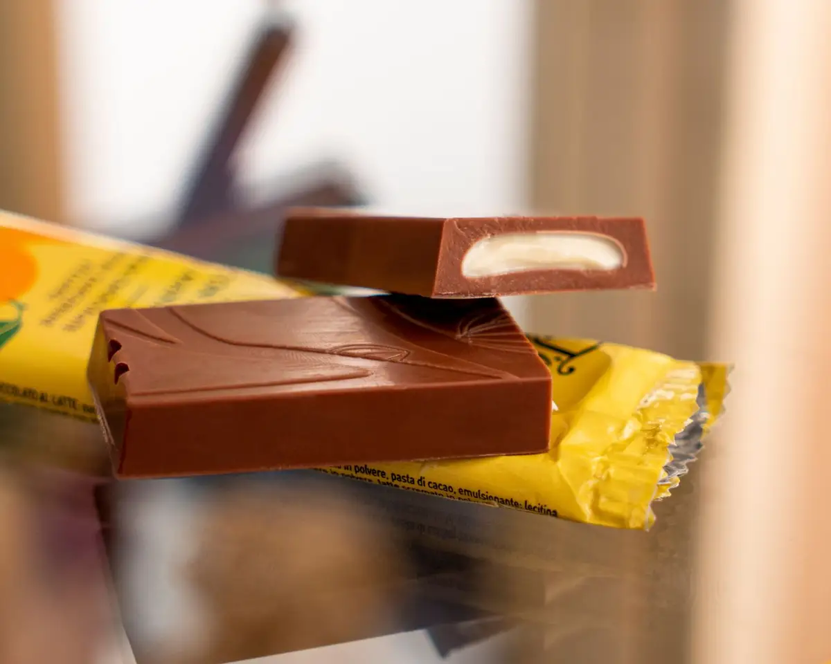 Una tavoletta di cioccolato al latte spezzata, col ripieno chiaro, sulla sua carta gialla